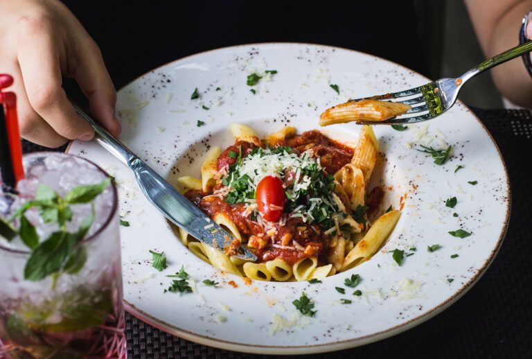 man eating bolognese penne pasta garnished with herbs